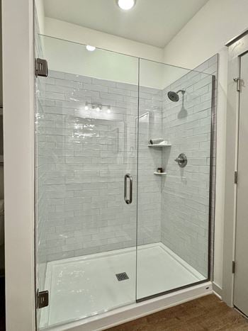 A glass shower stall with a white door and a white tiled wall